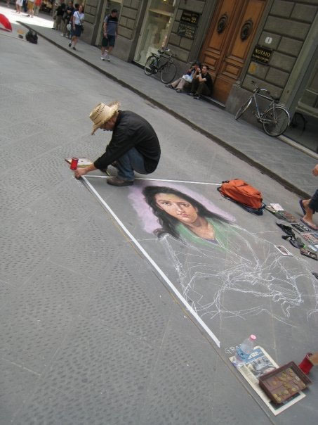 A picture of a man drawing in the Steets of Italy a picture of a woman.