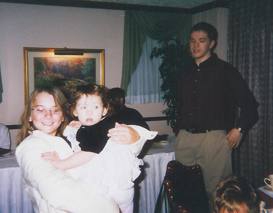 A child holding a baby with dad watching