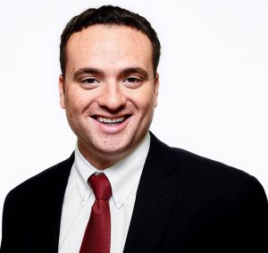 Portrait picture of Shawn Mulvey smiling and wearing black suit and red tie